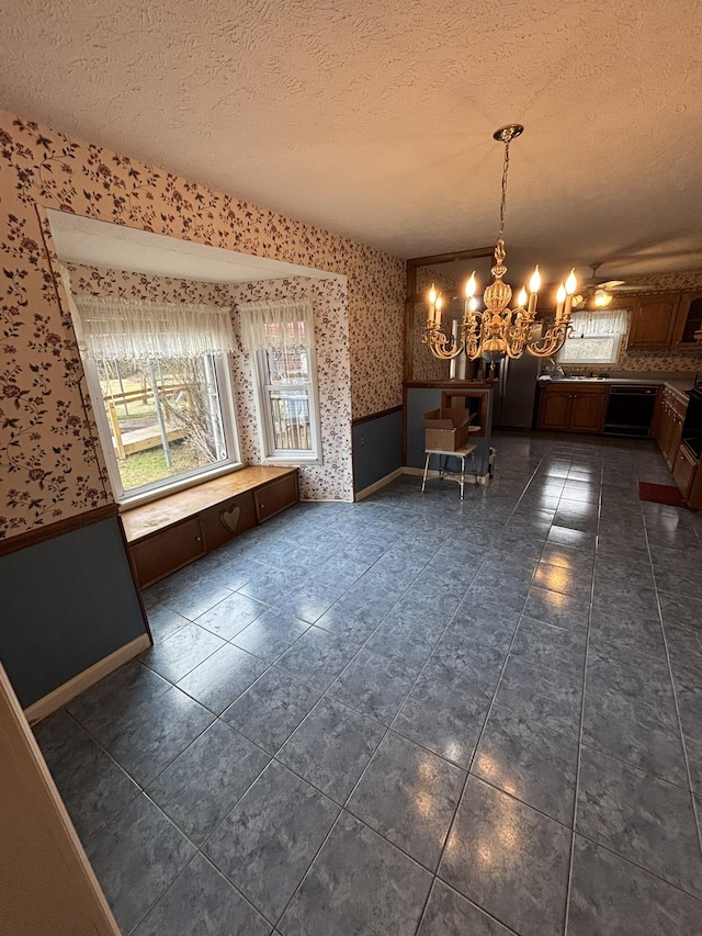 unfurnished dining area with dark tile patterned floors, ceiling fan with notable chandelier, and a textured ceiling