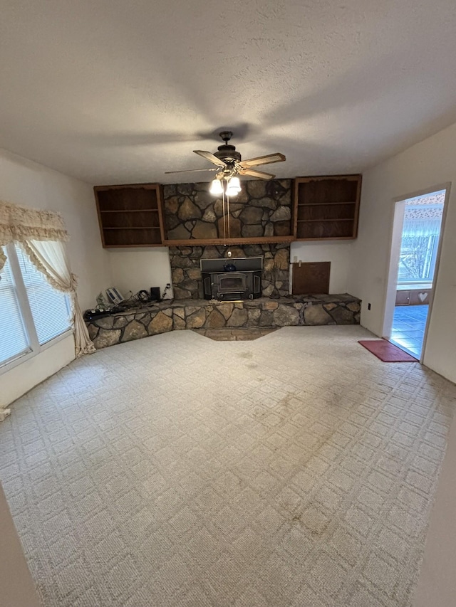 unfurnished living room featuring ceiling fan, a wood stove, and a textured ceiling