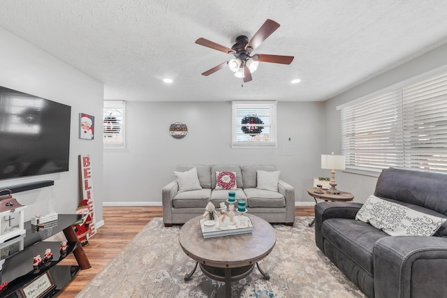 living room featuring ceiling fan, light wood-type flooring, and a textured ceiling