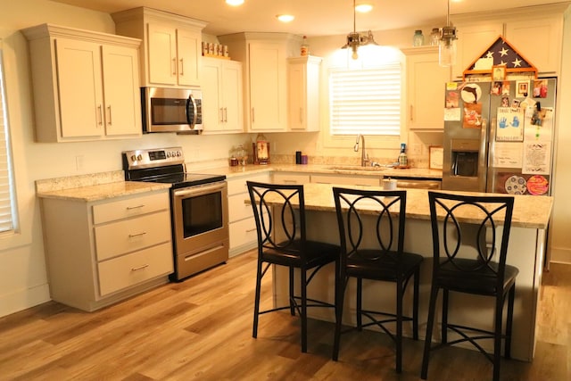 kitchen featuring appliances with stainless steel finishes, sink, a kitchen island, hanging light fixtures, and a breakfast bar area