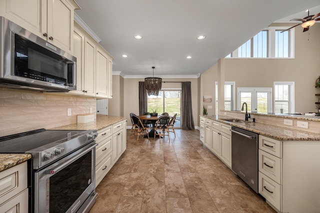 kitchen featuring cream cabinetry, appliances with stainless steel finishes, light stone counters, and hanging light fixtures