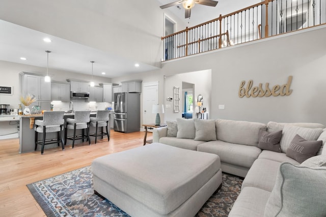 living room featuring ceiling fan, a towering ceiling, sink, and light hardwood / wood-style flooring