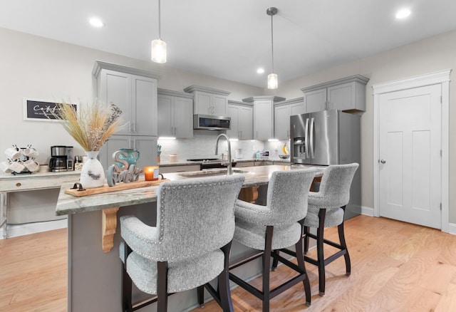 kitchen with light hardwood / wood-style floors, light stone countertops, pendant lighting, and appliances with stainless steel finishes