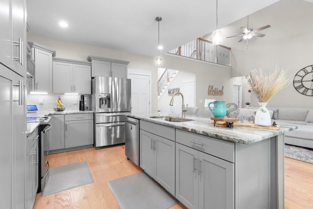 kitchen with appliances with stainless steel finishes, light wood-type flooring, ceiling fan, sink, and a center island with sink