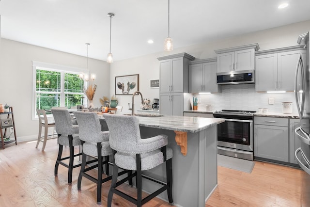 kitchen featuring a kitchen island with sink, sink, light hardwood / wood-style flooring, light stone countertops, and appliances with stainless steel finishes