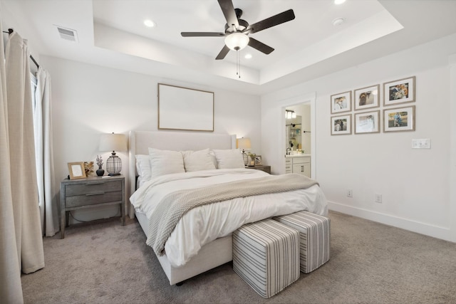 carpeted bedroom with ensuite bath, a raised ceiling, and ceiling fan