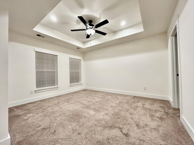 empty room with ceiling fan, a raised ceiling, and light colored carpet