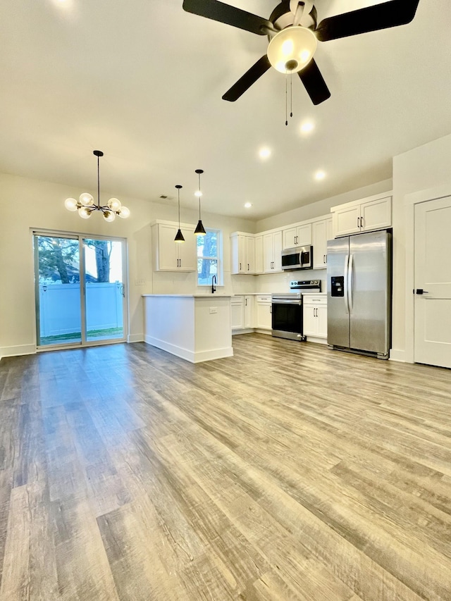 kitchen with pendant lighting, ceiling fan with notable chandelier, stainless steel appliances, and white cabinetry