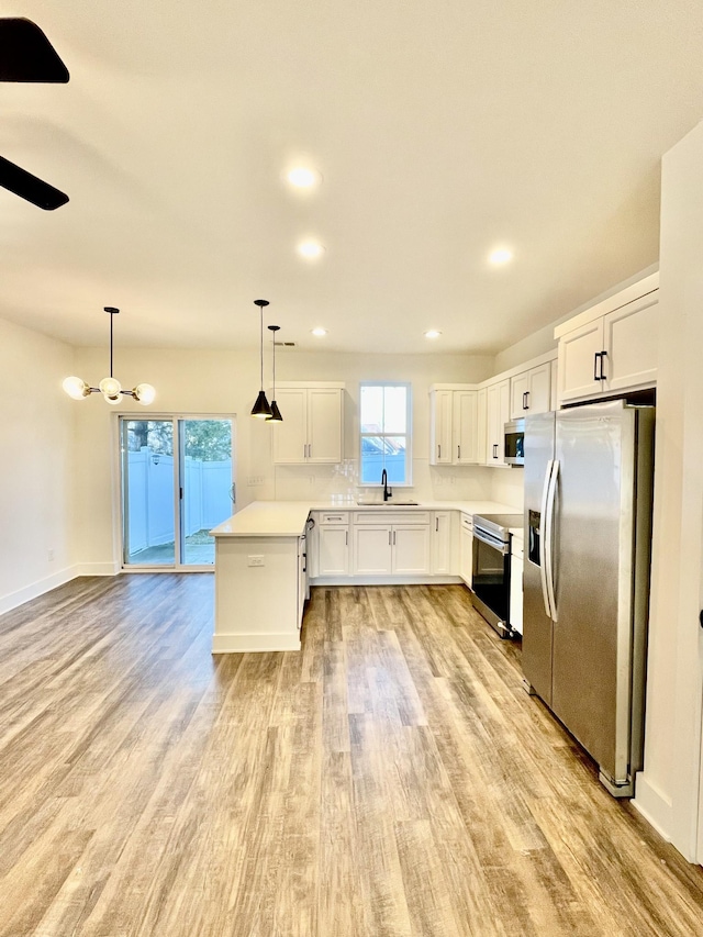 kitchen with white cabinets, light wood-type flooring, decorative light fixtures, and appliances with stainless steel finishes