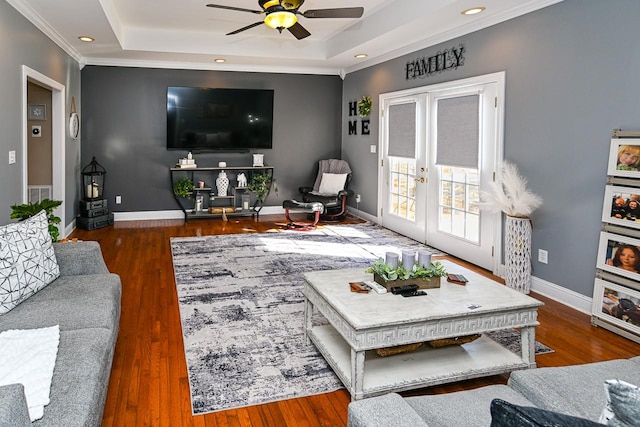 living room with french doors, a tray ceiling, dark wood-type flooring, and crown molding