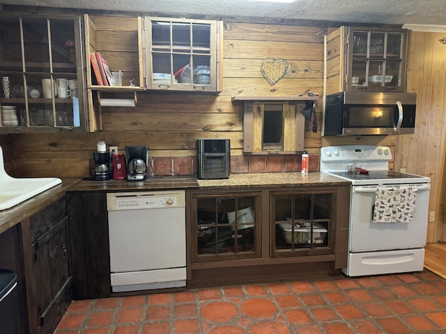 kitchen featuring a textured ceiling, wooden walls, and white appliances