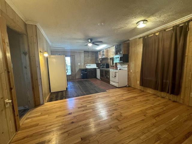 kitchen featuring dark hardwood / wood-style flooring, wood walls, crown molding, a textured ceiling, and white appliances