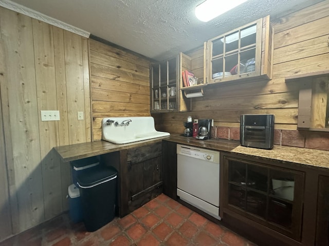 kitchen with a textured ceiling, sink, dark tile patterned flooring, dishwasher, and wood walls