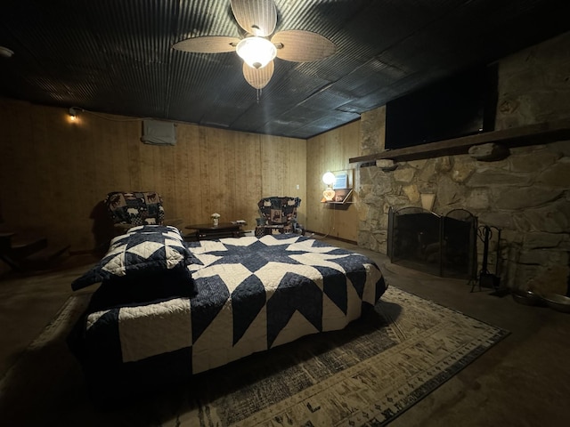 bedroom with ceiling fan, a fireplace, wooden walls, and concrete floors