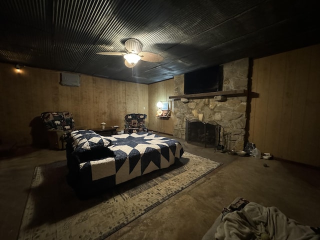 bedroom with a stone fireplace, ceiling fan, concrete floors, and wood walls