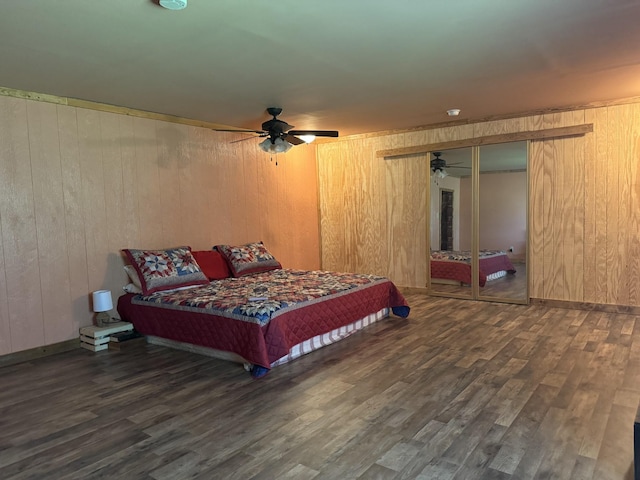 bedroom featuring ceiling fan, dark hardwood / wood-style flooring, and wooden walls