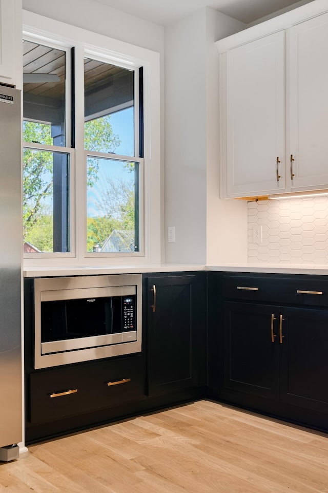 kitchen with light wood-type flooring, stainless steel appliances, white cabinetry, and backsplash