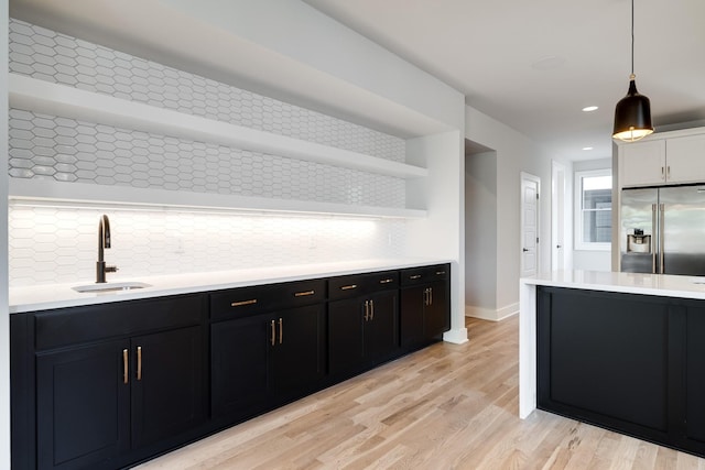 kitchen with sink, stainless steel refrigerator with ice dispenser, backsplash, pendant lighting, and light hardwood / wood-style floors