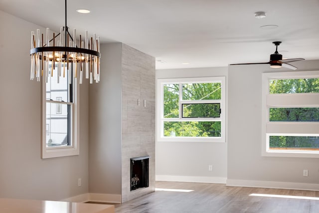 unfurnished living room with ceiling fan with notable chandelier, a tile fireplace, a wealth of natural light, and light hardwood / wood-style flooring