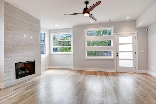 unfurnished living room with ceiling fan, light wood-type flooring, and a tile fireplace