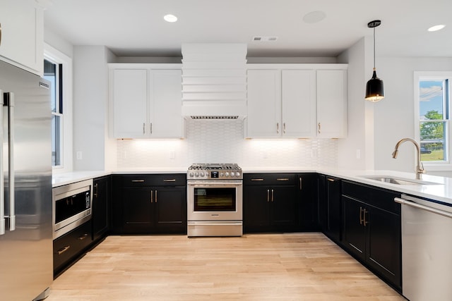 kitchen with appliances with stainless steel finishes, sink, decorative light fixtures, light hardwood / wood-style flooring, and white cabinets