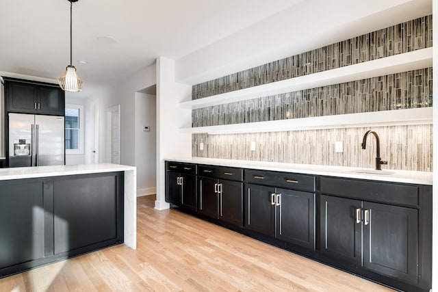 kitchen with high end refrigerator, sink, pendant lighting, and light hardwood / wood-style floors