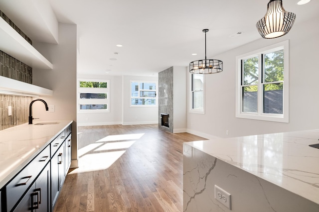 kitchen featuring light wood-type flooring, light stone counters, a large fireplace, sink, and pendant lighting