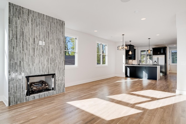 unfurnished living room with sink, light wood-type flooring, a fireplace, and a chandelier