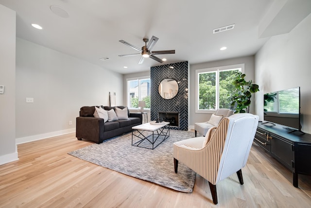 living room with ceiling fan, light wood-type flooring, and a tile fireplace