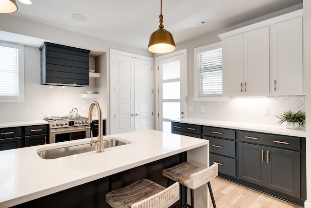 kitchen featuring high end range, light wood-type flooring, white cabinetry, hanging light fixtures, and a breakfast bar area