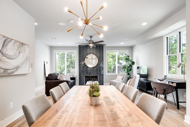 dining area with light wood-type flooring, an inviting chandelier, a healthy amount of sunlight, and a tiled fireplace