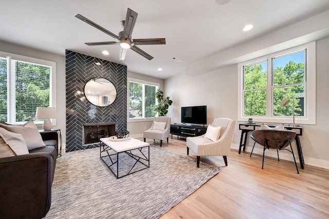 living room with plenty of natural light, ceiling fan, a fireplace, and light hardwood / wood-style flooring