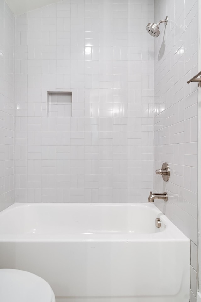 bathroom with toilet, tiled shower / bath, and vaulted ceiling