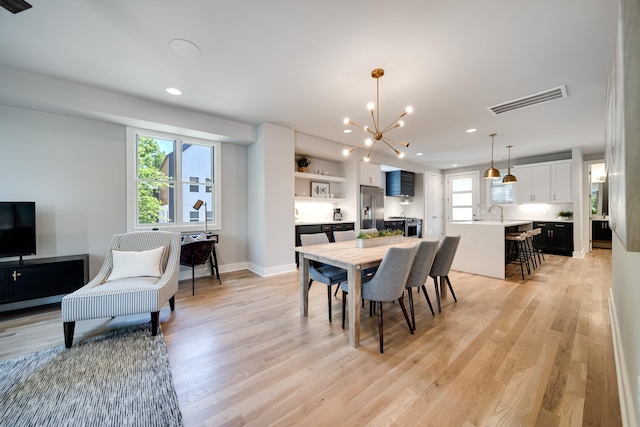 dining area with light hardwood / wood-style floors, plenty of natural light, a notable chandelier, and sink