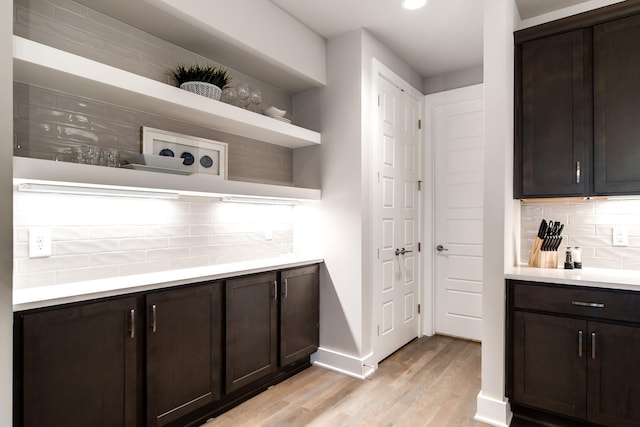 kitchen with dark brown cabinets, light wood-type flooring, and tasteful backsplash