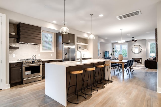 kitchen featuring hanging light fixtures, stainless steel appliances, a kitchen island with sink, and range hood