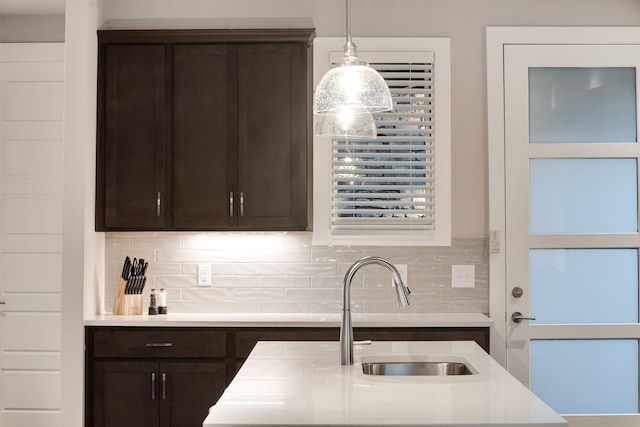 kitchen featuring decorative backsplash, dark brown cabinets, hanging light fixtures, and sink