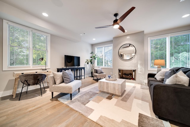 living room featuring ceiling fan, a fireplace, and light wood-type flooring