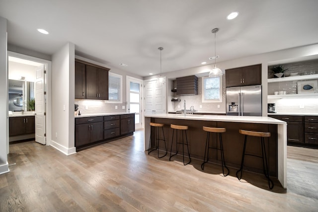 kitchen with sink, an island with sink, high quality fridge, dark brown cabinets, and light hardwood / wood-style floors