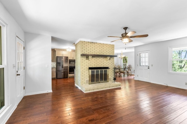 unfurnished living room featuring a fireplace, dark wood-type flooring, and ceiling fan with notable chandelier