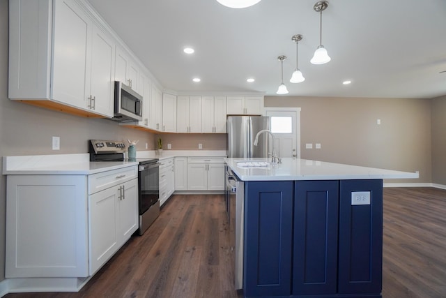 kitchen featuring dark wood-type flooring, an island with sink, pendant lighting, white cabinets, and appliances with stainless steel finishes