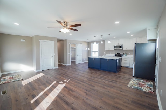 kitchen featuring appliances with stainless steel finishes, a barn door, decorative light fixtures, white cabinetry, and an island with sink