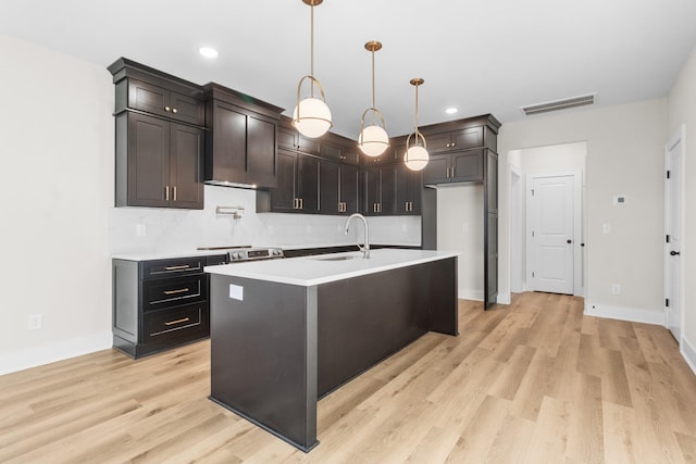 kitchen featuring pendant lighting, light wood-type flooring, a kitchen island with sink, and sink