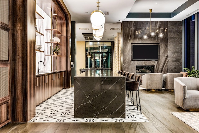 bar featuring a chandelier, sink, light hardwood / wood-style flooring, and a high end fireplace