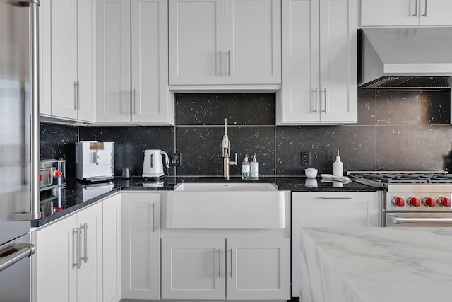 kitchen featuring dark stone counters, white cabinets, wall chimney range hood, appliances with stainless steel finishes, and tasteful backsplash