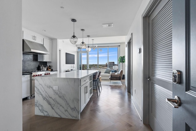 kitchen with a center island, hanging light fixtures, white cabinets, decorative backsplash, and high end range