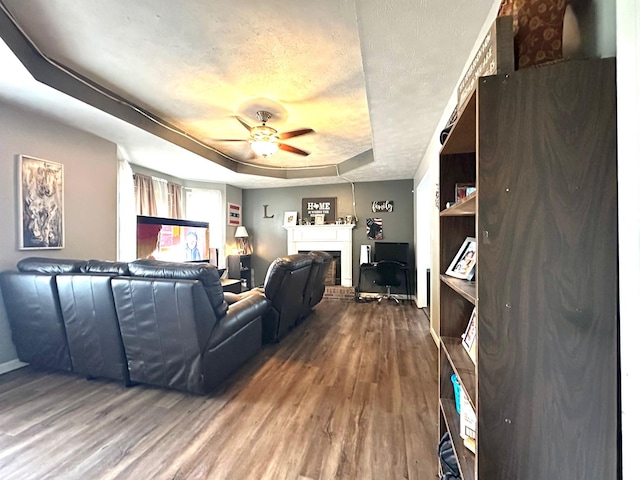 living room with a raised ceiling, a brick fireplace, hardwood / wood-style flooring, ceiling fan, and a textured ceiling