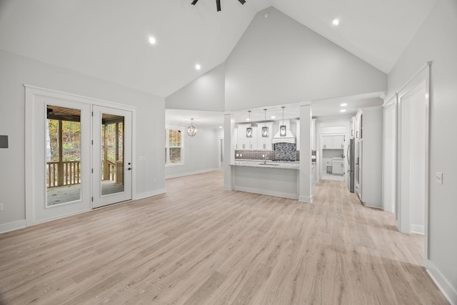 unfurnished living room featuring sink, high vaulted ceiling, ceiling fan with notable chandelier, and light wood-type flooring