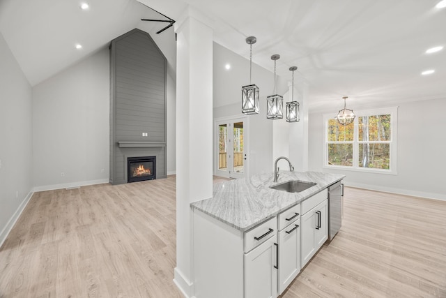 kitchen with white cabinetry, a large fireplace, sink, light stone counters, and vaulted ceiling