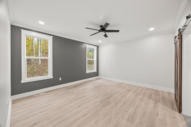 spare room featuring a barn door, light hardwood / wood-style flooring, a wealth of natural light, and crown molding